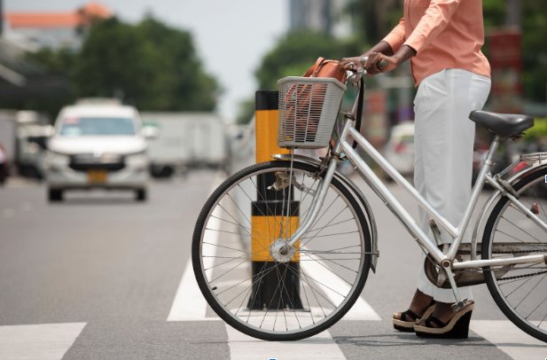 Mujer esperando cruzar una calle con su bicicleta, quien podría necesitar un abogado de accidentes en bicicleta.